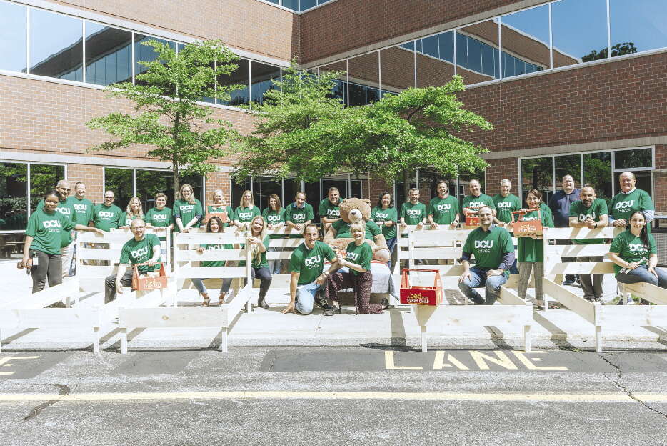 A large group of DCU credit union employees stand with bed frames.