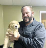 A man wearing a blue shirt holds a puppy.