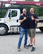 Two men embrace each other in front of a Sunshine Sign Co. truck