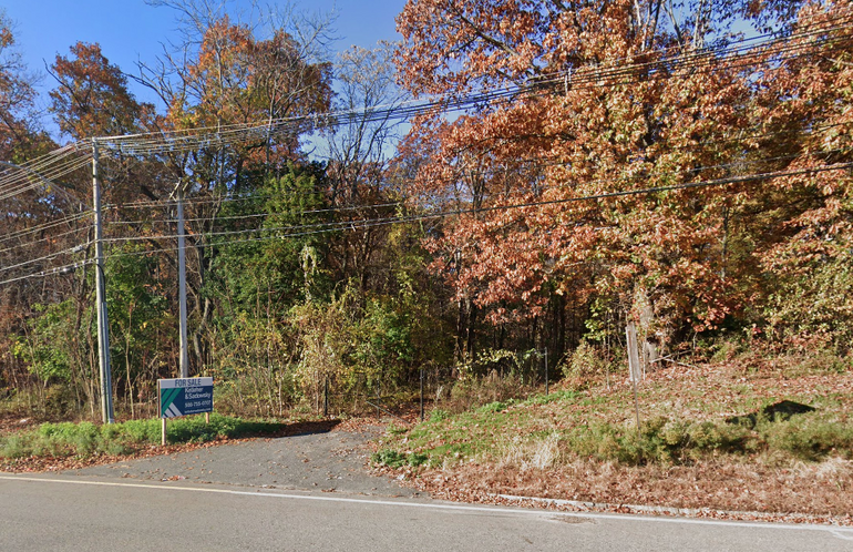 A wooded area with a real estate sign in front