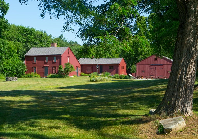 Three red wooden house and barn structures behind a trimmed, grassy yard