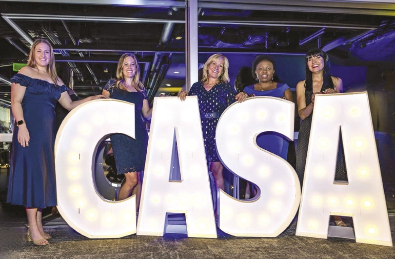 Five women standing behind large letter cutouts that spell C-A-S-A