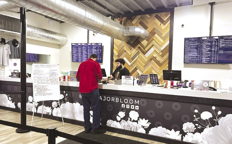 A customer and a cashier stand at a retail counter inside a cannabis dispensary.