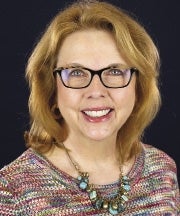 A woman wearing glasses, a multicolor sweater, and blue necklace