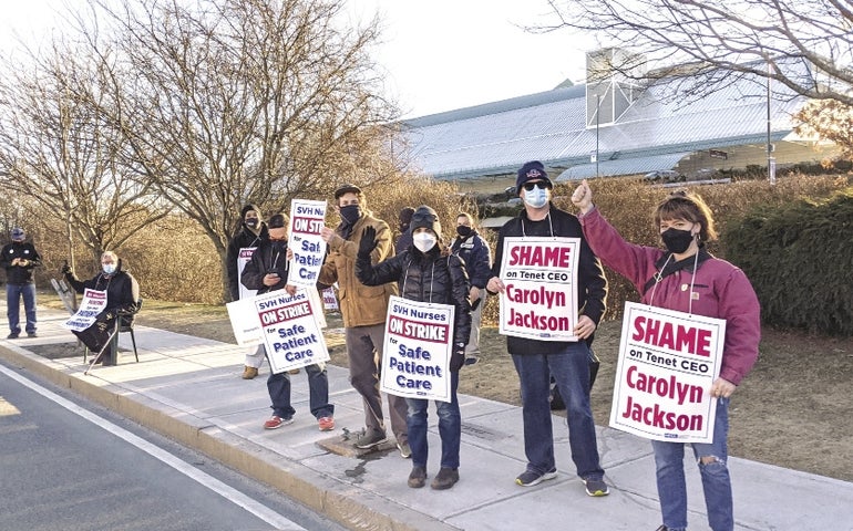 People stand on a sidewalk holding signs in front of Saint Vincent Hospital