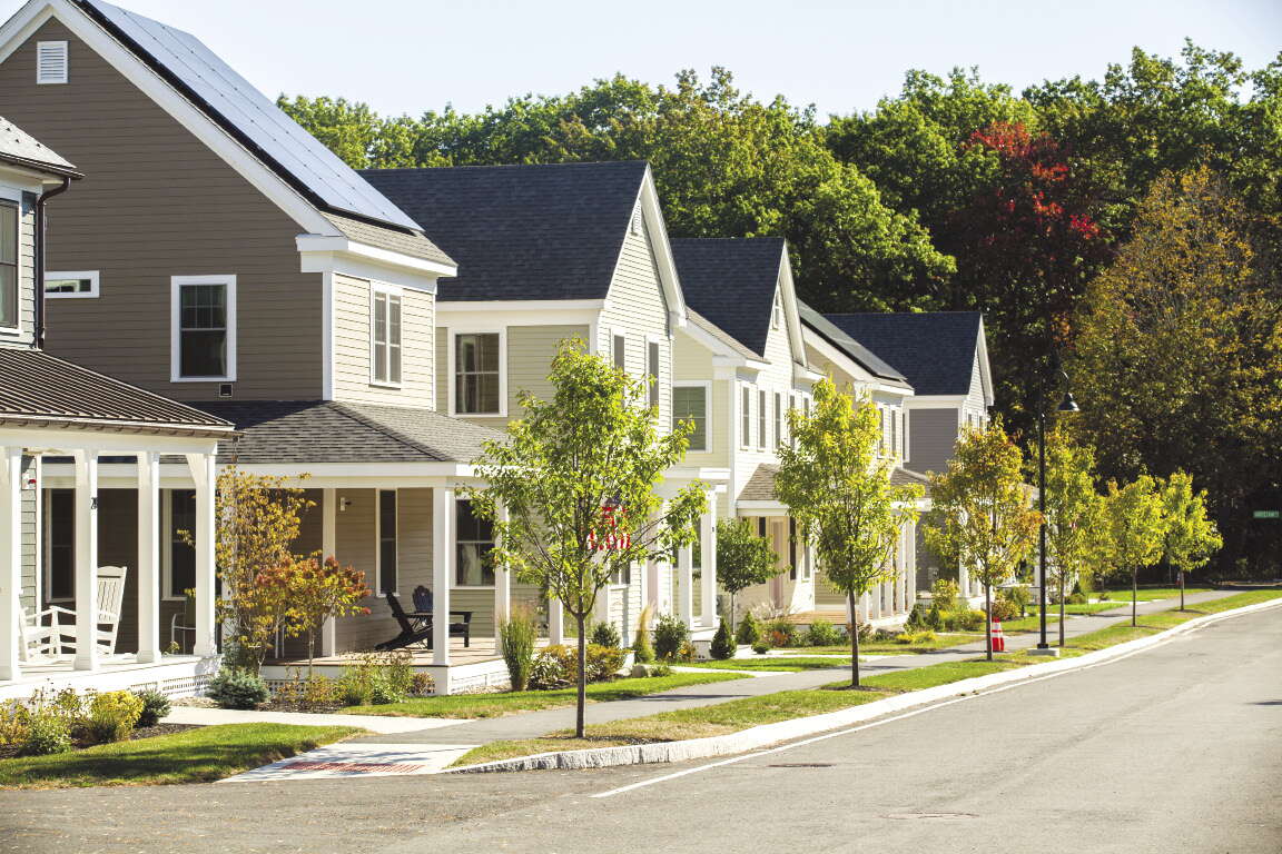 A row of houses with a sidewalk and trees in front of it along a street