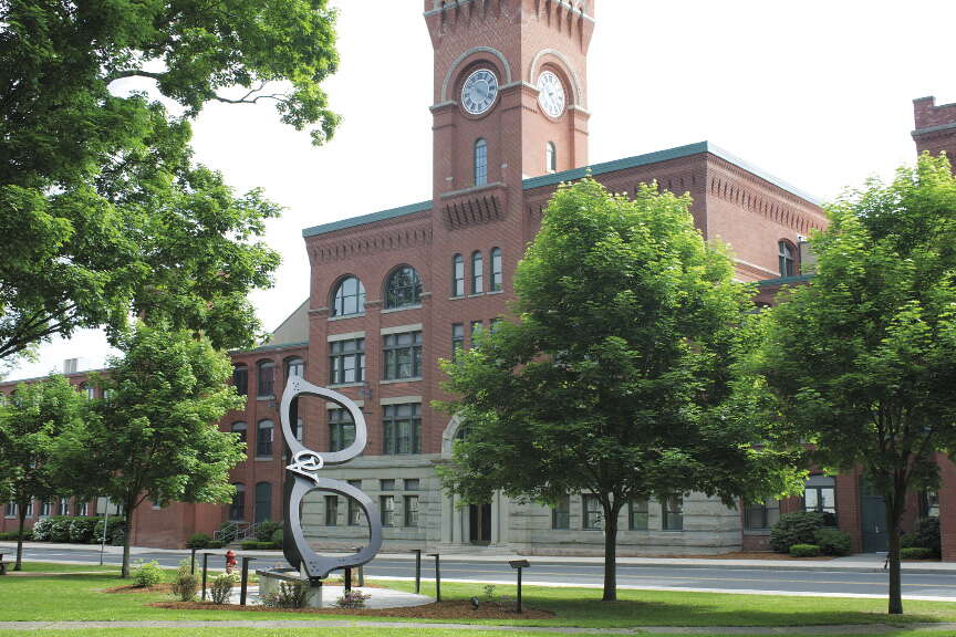 A brick building with a tower and a large sculpture of black glasses standing sideways with trees around it