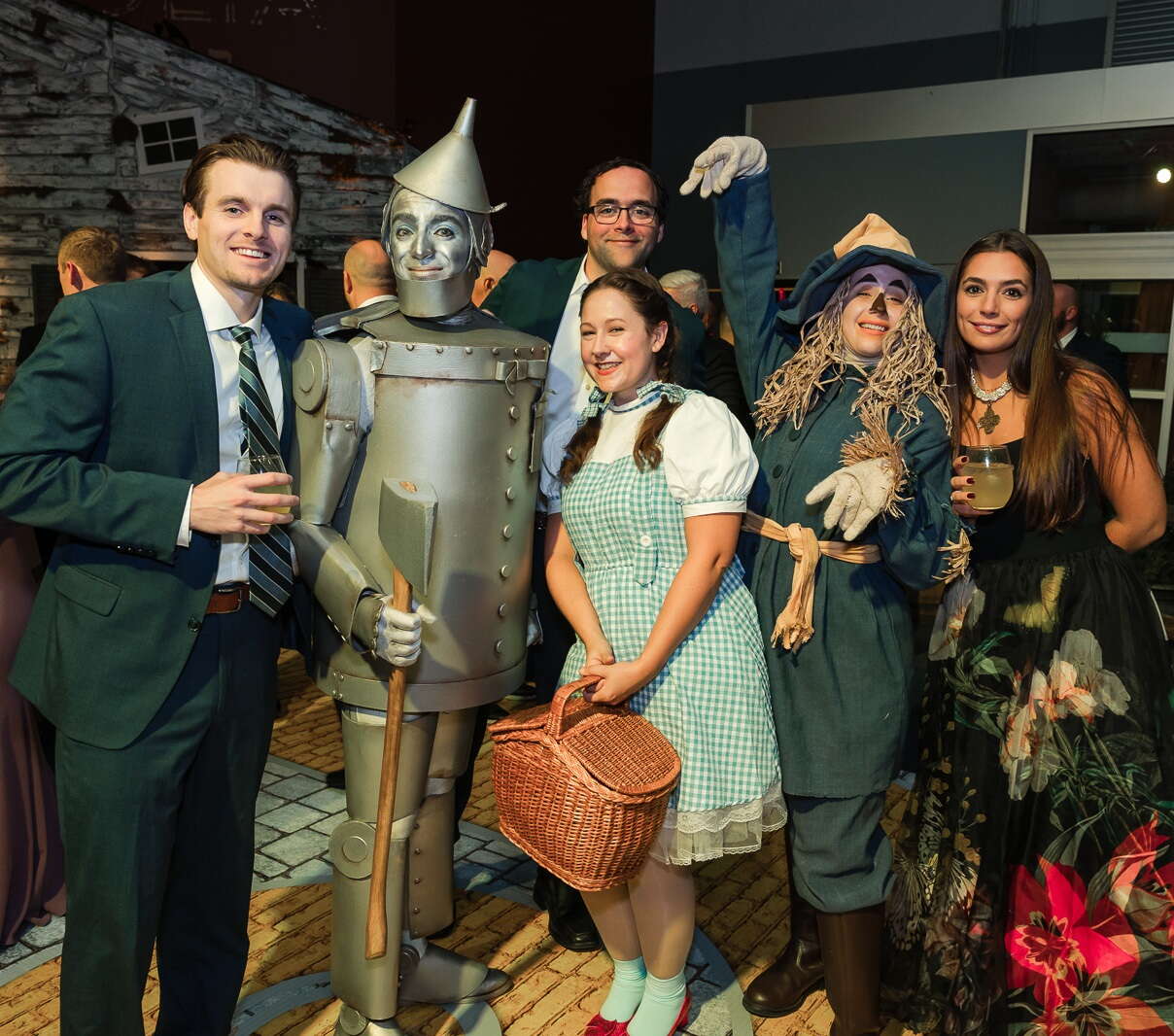 A group of people stand around The Wizard of Oz characters including the Tin Man, Dorothy, and the Cowardly Lion.