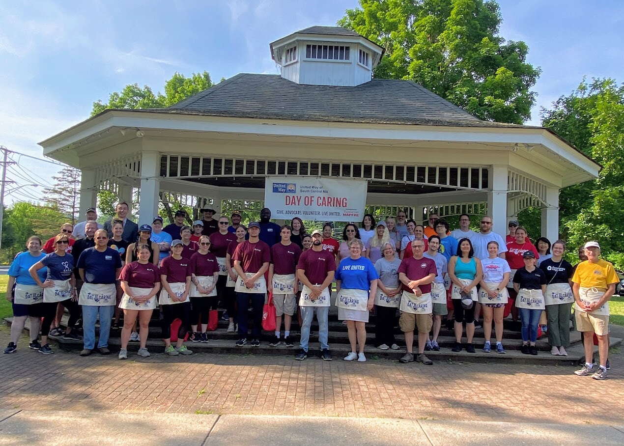 A group of people stand wearing white aprons in a brick sidewalk underneath a large gazebo.