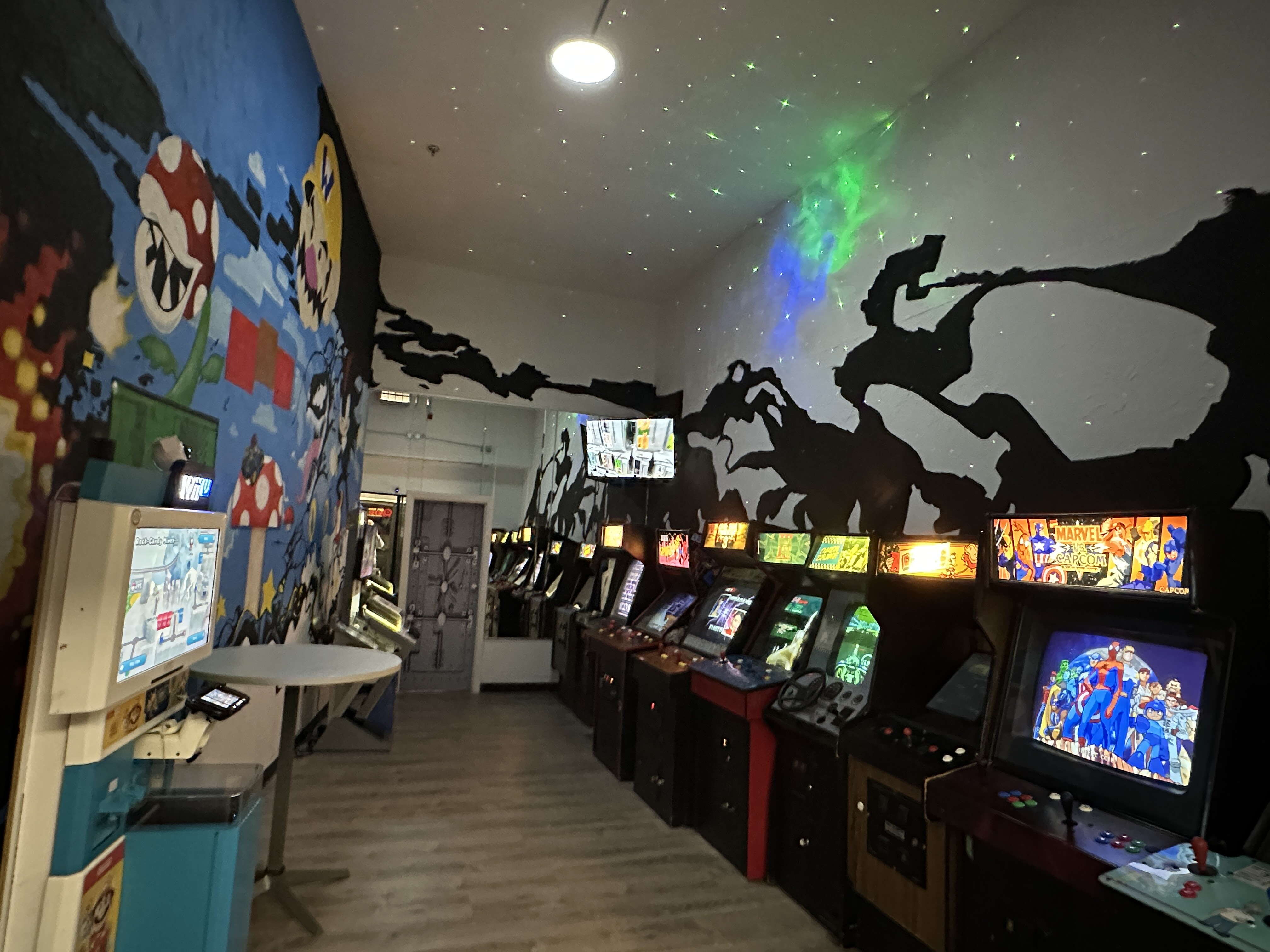 Arcade cabinets line the wall of a room with murals