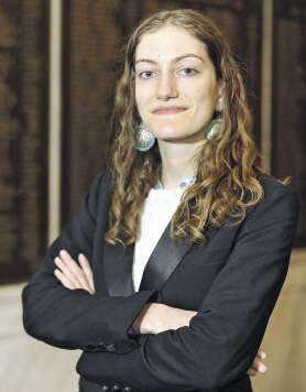 A woman stands in a suit arms crossed with circular earrings