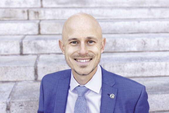 A man smiles at the camera, wearing a blue suit and tie.