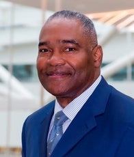 A man with in a blue suit jacket, a white and blue striped shirt, and a blue tie.