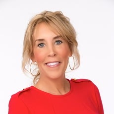 A headshot of a woman with blond hair tied back and bangs wears gold hoop earrings and a red blouse.