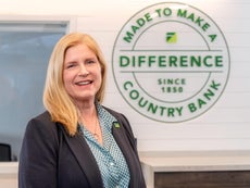 A woman in a suit jacket stands in front of a logo on a wall