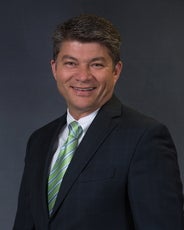 A smiling man wears a black suit with a green tie