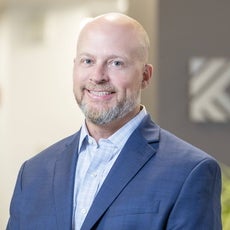 A man with a beard wears a blue shirt and a blue jacket