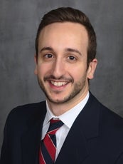 A man wearing a blue-and-red striped tie smiles at the camera.