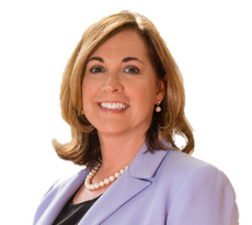 A woman wearing a purple blazer, a black shirt, and a pearl necklace smiles at the camera.