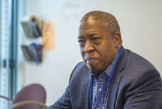 A man in a blue patterned suit jacket, white and blue checkered tie with a blue lanyard around his neck.