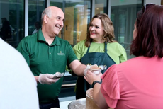 A man in a green shirt and a woman in a lime green shirt and green apron serve ice cream