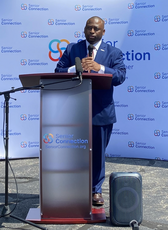 A man stands at a podium outside on concrete. 