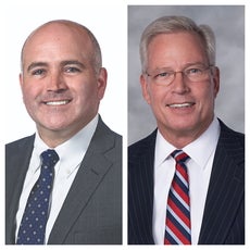 Side by side headshots of two men. The man on the left wears a grey suit jacket, white button down, and blue patterned tie while the man on the right wears a black pinstriped suit, a white button down, and blue, red, and white striped tie