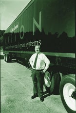 A man stands with his hands on his hips in front of a large tractor trailer with "AViiON" printed on the side.