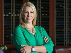 A woman with blonde hair stands with her arms crossed wearing a light green blouse