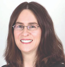 A woman with shoulder length brown hair wears thin wire-framed glasses.