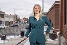 A woman in a green suit stands in front of a small downtown setting