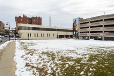 An empty lot with a parking garage featuring a mural and another building with a mural behind it. 