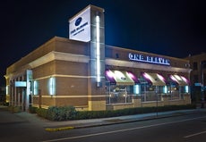 Outside a brick building housing a restaurant with a light-up sign reading "ONE ELEVEN" above three awnings shading three windows