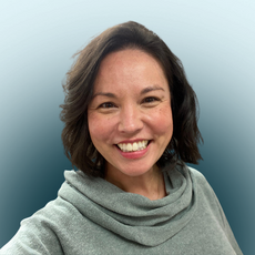 A woman with shoulder length dark brown hair wears a light green cowl neck sweater.