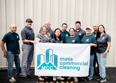 Eleven people stand holding a white banner reading "mass commercial cleaning".