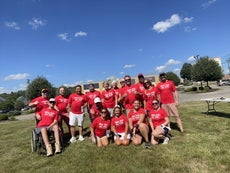 17 people sit and stand in red t-shirts on a grassy field.