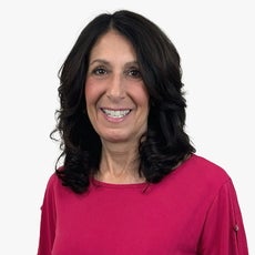 A woman with dark wavy hair wears a bright pink top.