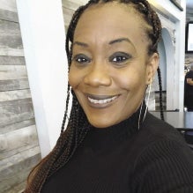 A woman with long braids wears a black turtleneck sweater.