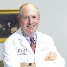 A man in a white lab coat stands with crossed arms and smiles for the camera