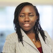 A woman with dark braids wears a pinstripe suit jacket.