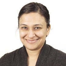 A woman with her dark hair pulled back wears a black top and smiles for the camera.