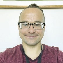 A man wears black rimmed glasses and a maroon shirt.