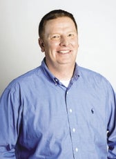 A man smiles while wearing a blue button-up shirt