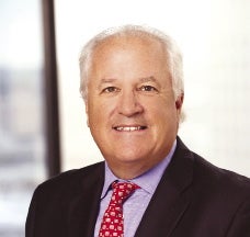 A man with white hair wears a black suit jacket, light purple button down, and red patterned tie.