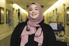 A woman wears a black top and a light mauve head wrap with a stethoscope hanging around her neck. 