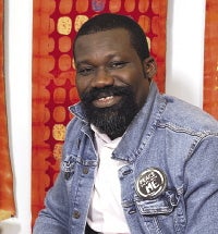 A man with a dark beard wears a jean jacket and white polo shirt.