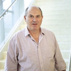 A man in a checkered button down stands in front of a white stairwell.