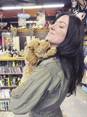 A woman with long dark hair and a green jacket holds a brown puppy up to her face.