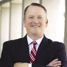 A man in a black suit and red and white striped tie with crossed arms