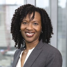 A woman wears a grey suit jacket and white blouse.